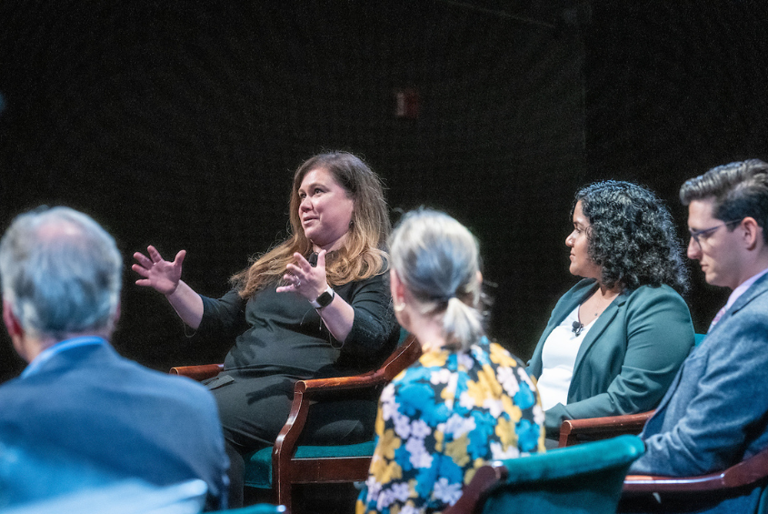 Faculty sitting on a stage, talking with each other